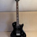 Černá elektrická kytara s dvojstupňovitým tělem a tmavým hmatníkem. Na hlavě je viditelné logo "Epiphone". Hmatník obsahuje bílé vložky ve tvaru pták…