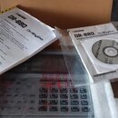 Na fotografii je elektronický bubeník v přepravním kartónu s polystyrenovými výplněmi. K přístroji patří uživatelský manuál s nápisem „BOSS DR-880 Dr…