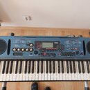 Modrý digitální klavír značky YAMAHA s modelem DJX. Nástroj má standardní klávesnici a ovládací panel s displejem, několika posuvníky, tlačítky a kno…