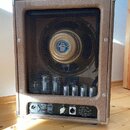 Kytarový zesilovač v hnědém koženěném potahu s kovovými rohy. Přední mřížka odhaluje reproduktor a v dolní části viditelné elektronkové koncovky. Na…