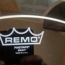 Černý bubnový kožen s bílým nápisem. Je na něm viditelné logo REMO v rámci stylizované koruny a text PINSTRIPE® EBONY® MADE IN U.S.A. Povrch je leskl…