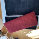 Otevřený hliníkový kufr s černým vnitřkem. Uvnitřku leží obdélníkový předmět potažený červeným texturovaným materiálem připomínajícím koberec. Na fot…