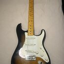Elektrická kytara s tónem těla v provedení sunburst a bílým pickguardem. Na hlavě hředu je viditelné logo Fender. Nástroj má javorový hmatník a tři s…