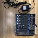 Černý mixážní pult s nápisem PHONIC AM460DP. Zařízení obsahuje několik vstupních kanálů s potenciometry a přepínači, pravá strana má výstupy pro XLR…