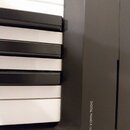 Detailní záběr na klávesy digitálního piana v černé barvě. Na šasi je bílý nápis DIGITAL PIANO P-145 a v horní části částečný nápis BOOST on/off. Pov…