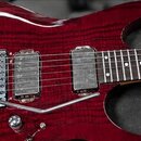 Detail elektrické kytary s červeným lakovaným tělem s viditelnou strukturou dřeva. Nástroj má dva humbuckery, hrazivý kobylník s páčkou a hnedý hmatn…