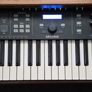 Černý MIDI kontrolér s klaviaturaí. Na levé straně je nápis KEYLAB 61 ESSENTIAL a uprostřed logo ARTURIA. Horní panel obsahuje podsvícené tlačítka, f…