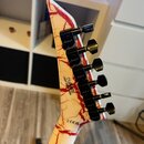 Hlava elektrické kytary s bílým povrchem a červenými žilkami připomínající mramor. Na zadní straně jsou černé ladičky s nápisem jackson na každém mec…