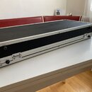 Černý obdélníkový přepravní kufr s hliníkovým profilem a kovovými rohy. Na boku jsou vidět dvě černé kulaté úchytky a kovové zámky. Povrch kufrů je p…