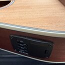 Detail akustické kytary s dřevěnou deskou a tmavšími boky. Na boku je umístěn černý plastový panel s ovládacími prvky a nápisy LOW, MID, TREBLE, VOLU…