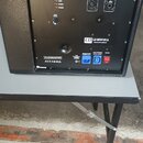Černý aktivní subwoofer s texturovaným povrchem. Na zadním panelu je nápis LD MON121A a logo LD Systems. Panel obsahuje ovládací prvky, konektory INP…