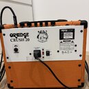 Zadní strana oranžového kytarového komba s bílým zadním panelem. Na panelu je nápis ORANGE CRUSH 20 a štítek s textem ORANGE, model CRUSH 20, TYPE GU…