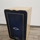Dřevěný cajon světlé barvy s černým předním panelem. V dolní části panelu je bílý nápis „Marcel Anton Edition“ a pod ním texty „HANDMADE IN AUSTRIA“,…
