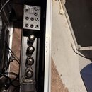 V hliníkovém transportním kufru se nachází černý rackový zesilovač s čtyřmi elektronkami v řadě. Na horním ovládacím panelu jsou čtyři otočné potenci…