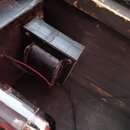 Detail vnitřku zařízení s černým transformátorem, který je připevněn k šasi. K transformátoru vedou červený a černý vodič. V popředí je vidět část sk…