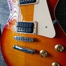 Elektrická kytara s červeno-žlutým gradientním lakem a bílým plechtrátem. Nástroj má dva humbuckery s černými snímači, chromovaný most a čtyři zlaté…