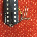 Černý humbucker s dvěma řadami šesti bílých pólů. Na levé straně je nápis R.M.pickups. K snímači vedou elektrické vodiče a vedle něj jsou položeny dv…
