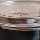 Detailní pohled na horní část bubnu s průhledným tělem a chromovaným obručím. Na bláně je vidět logo REMO a nápis PINSTRIPE. Na vnější straně obruče…