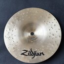 Kovový činel s hammeringem (důlky v povrchu) a jemným žilováním. V dolní části je čitelné logo Zildjian. Povrch vykazuje známky opotřebení a znečiště…