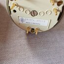 Fotografie zachycuje spodní část bílého kulatého zařízení s několika zlatými kontakty. Na bílém štítku je uveden nápis KK 87s 25113 a Made in Germany…