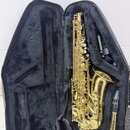 Zlatý saxofon v černém polstrovaném kufru. Na zvonu nástroje je nápis "YAMAHA". V kufru je vedle saxofonu umístěn munčník s nápisem "YAMAHA" a černý…
