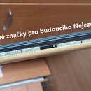 Detailní pohled na hmatník strunového nástroje s jasnou dřevěnou barvou. Na hmatníku jsou umístěny bílé papírové nebo plastové značky s modrými svisl…