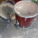 Dva červené bubny s kovovými obručmi a napínacími šrouby. Na blánách je vidět logo REMO. Jeden z bubnů má na boku zlatý nápis 70s. K nástrojům patří…