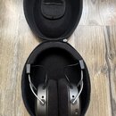 Černé sluchátka s šedými vnějšími mušlemi jsou umístěna v černém přepravním pouzdře. Na pravé mušli je viditelný USB-C konektor. Nástroj nemá žádné č…