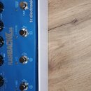 Modrý kytarový efekt s bílým rámem. Na horní straně je nápis FLASHBACK DELAY AND LOOPER a logo tc electronic. Zařízení má čtyři černé otočné knoflíky…