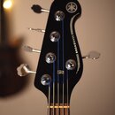 Černá hlava basové kytary s nápisem BROADBASS a logem značky Yamaha. Na hlavě jsou umístěny čtyři kovové ladičky a modré struny. Povrch je hladký a v…