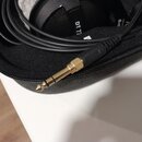 Černý kabel s pozlaceným 6,3mm jack konektorem v černém zipovém pouzdře. V pozadí jsou vidět části černých sluchátek s bílým nápisem DT 77. Povrchy j…