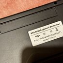 Detail spodní strany černého plastového zařízení. Na bílé nálepce je text USB MIDI Keyboard Controller, symbol USB a značky CE, FC a přeškrtlená koš.…