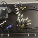 Sada kabeláže a elektroniky v hliníkovém přepravním kufru s černým dnem. V levé části je šedý box s červeným prvkem s nápisem TIP-TAP a černým prvkem…