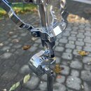 Detail chromovaného kovového stojanu s úchytem. Povrch je lesklý, v některých místech jsou viditelné drobné škrábance a nečistoty. Na fotce nejsou žá…