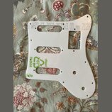 Bílá plastová pickguard pro kytaru s několika otvory a výřezy. Na povrchu jsou viditelné zelené nápisy „sheet“, „Side“ a symbol recyklace s číslem „0…