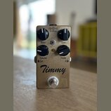 Kytarový efekt pedál v bronzové barvě s kovovým povrchem. Na přední straně jsou čtyři černé otočné knoflíky s popisky Bass, Gain, Volume a Treble. Up…