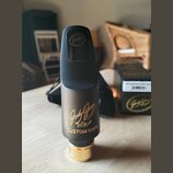 Černý saxofonový mouthpiece s matným povrchem a zlatým kovem v dolní části. Na přední straně je zlatý nápis „Jody Jazz HR* CUSTOM DARK“. V horní část…