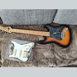 Elektrická kytara s tělem v provedení sunburst a hnědým hřebenatým pickguardem. Na hlavě je viditelné logo Washburn. Vedle kytary leží v plastovém ob…