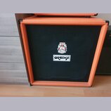 Kytarový reproduktor v oranžovém potahu s černou textilní mřížkou. Na mřížce je umístěno bílé obdélníkové logo s nápisem ORANGE a nad ním barevná nál…