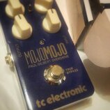 Modrý efekt pedál s nápisy MOJOMOJO, PAUL GILBERT OVERDRIVE a tc electronic. Na horní straně jsou tři krémové ovládací knoflíky a nápisy OUTPUT a INP…