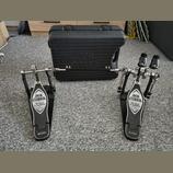 Dvojpedál na bicí buben v černé barvě s kovovými mechanismy a plastovým kufrem. Na obou šlapkách je bílý nápis IRON COBRA a pod ním kurzivou The Lege…