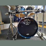 Modrá bicí souprava s chromovaným hardwarem a stojanem značky Millenium. Na přední straně basového bubnu je bílý nápis SINCE 2004 DC DRUMS QUALITY HA…