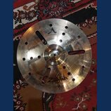Kovový činel s vryty a otvory v povrchu. Na povrchu je nápis CUSTOM a logo Zildjian. Činely vykazují známky používání v podobě drobných škrábanců a z…