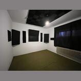 Fotografie znázorňuje místnost s akustickými panely. Na bílých stěnách jsou umístěny čtyři černé obdélníkové absorbéry různých velikostí a na stropě…