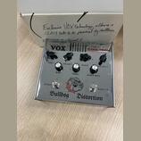 Stříbrný efekt pedál s nápisem Bulldog Distortion a logem hlavy buldoka. Na horním panelu je značka VOX a nápis COOLTRON TUBE TECHNOLOGY. Zařízení má…