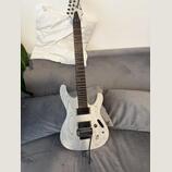 Elektrická kytara s bílým tělem a hnedem hmatníkem, vykazující výraznou zrnitu dřeva. Na hlavě je viditelné logo Ibanez. Nástroj má dva humbuckery, j…