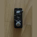 Černý kytarový pedál s nápisy MICRO ABY a Fender. Na horní části je vstup DC IN a přepínač CHANNEL SWITCH s označením A/B ● Y(A&B) a popisem A:RED, B…