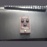 Obdélníkový efekt pedál v hnědé barvě s nápisy tc electronic a Rusty FUZZ. Na horní straně jsou tři černé ovládací knoflíky a červená kontrolka. V do…
