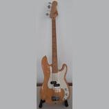 Elektrická basová kytara s přírodním dřevěným povrchem těla a hmatníkem. Na hlavě je viditelné logo "Fender". Instrument má bílý pickguard a čtyři st…