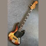 Elektrická basová kytara s dřevem hmatníku a tělem v přechodovém lakování od černé přes červenou po žlutou. Na hlavě je nápis "Fender JAZZ BASS". Čer…